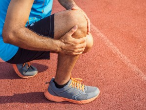 knee Injuries. sport man with strong athletic legs holding knee with his hands in pain after suffering muscle injury during a running workout training on Running Track. Healthcare and sport concept.