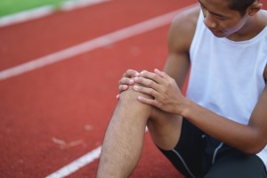 Picture of a man with an injured ACL sitting on a running track and holding his knee in pain.