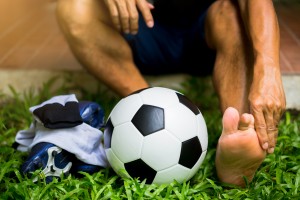 Picture of an injured soccer player sitting on the ground and holding his foot in pain.