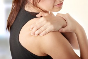 Picture of a woman with an injured rotator cuff touching her shoulder in pain.