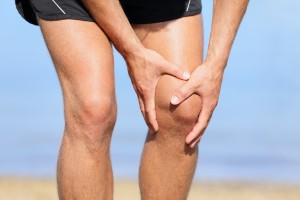 Picture of a man standing on a beach and holding his knee in pain.